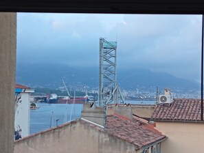 Blick auf eine Küstenstadt mit einer markanten Brücke, einem großen Frachtschiff und einer bergigen Kulisse.