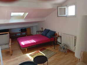 A compact bedroom with a single bed, a small table, a chair, a radiator, and a ceiling fan.