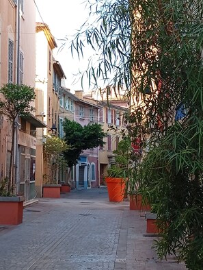 Eine schmale Straße gesäumt von Gebäuden, einem Baum und einem großen, orangefarbenen Blumenkasten.