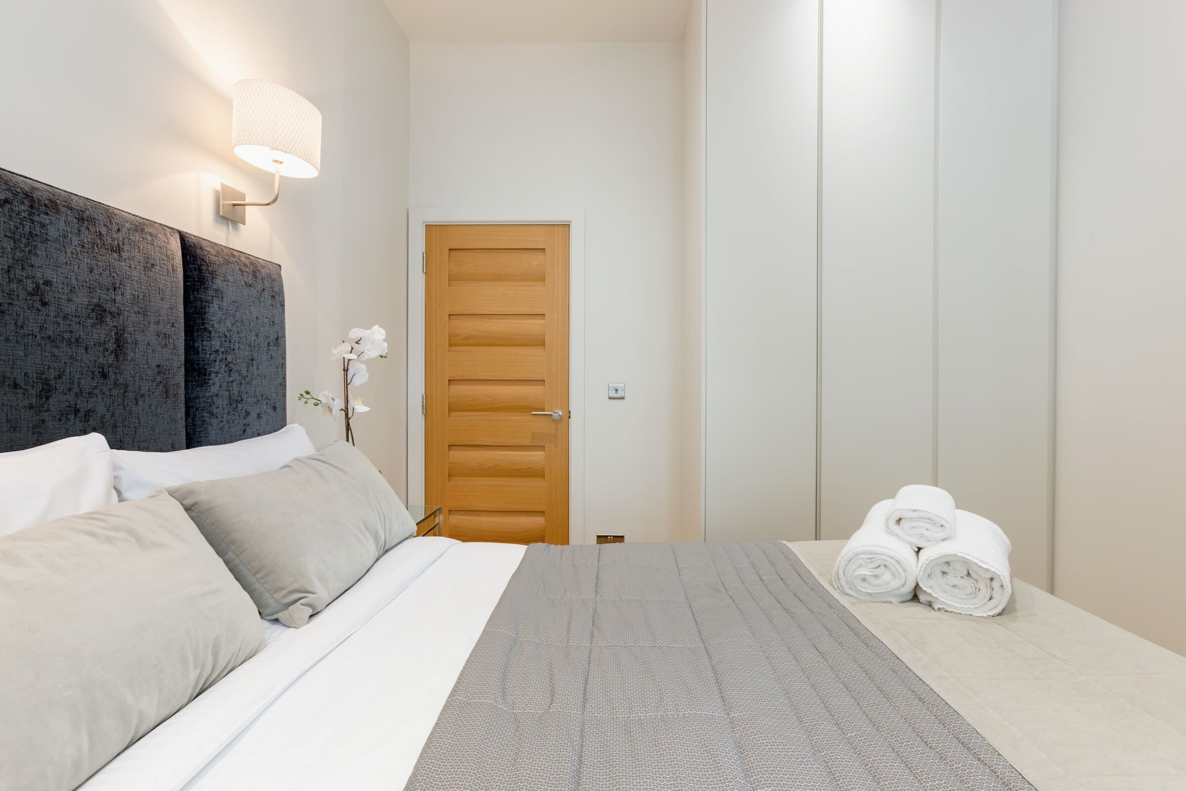 Une chambre d’hôtel avec un lit, une table de chevet, une lampe, une porte et un porte-serviettes avec des serviettes.