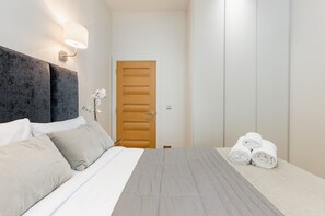Ein Hotelzimmer mit Bett, Nachttisch, Lampe, Tür und einem Handtuchhalter mit Handtüchern.