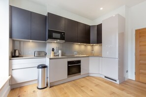 A modern kitchen with white cabinetry, a stainless steel microwave, a toaster, and a trash bin. - Modern Fitzrovia 3BR by Soho - London Centre (London)
