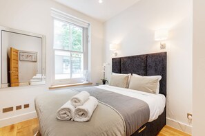 Ein modernes Schlafzimmer mit einem großen Bett, einem Fenster, einem Nachttisch und einem Spiegel.