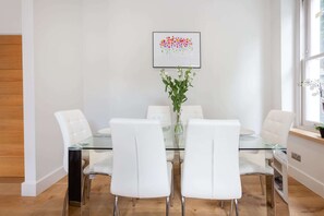 Un'area pranzo moderna con un tavolo in vetro, sedie bianche, un vaso con fiori e un quadro appeso al muro.