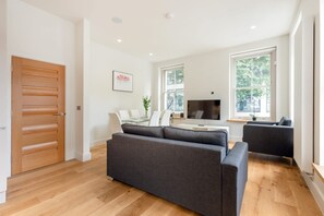 A modern living room with a sofa, a dining table with chairs, a TV, and large windows. - Modern Fitzrovia 3BR by Soho - London Centre (London)