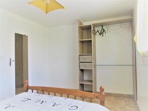 Een slaapkamer met een houten bed, een kledingkast met ophangruimte, en een deur naar een andere kamer.