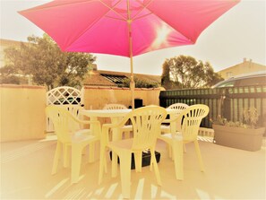 Een terras met een tafel, stoelen, een parasol en een hek.
