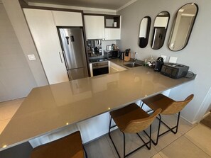 A modern kitchen with a central island, bar stools, stainless steel appliances, and a backsplash. -  Stunning 3-bedroom apartment in the heart of Sandton (Sandton)