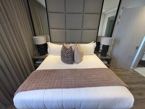 A hotel room with a large bed, a headboard, two bedside tables, and a mirror. -  Stunning 3-bedroom apartment in the heart of Sandton (Sandton)