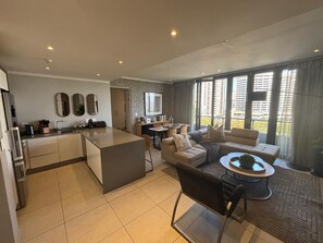 A modern apartment with a kitchen, dining area, and living room. There is a large window providing a view of the city. -  Stunning 3-bedroom apartment in the heart of Sandton (Sandton)
