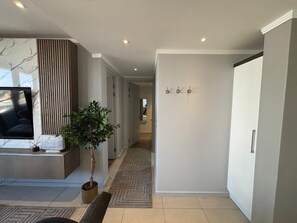 A modern hallway with a television, a potted plant, and a patterned rug. -  Stunning 3-bedroom apartment in the heart of Sandton (Sandton)