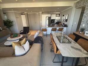 A modern living room with a sofa, coffee table, and dining area with chairs and a table. -  Stunning 3-bedroom apartment in the heart of Sandton (Sandton)