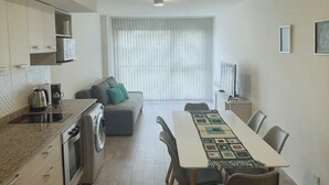 Eine moderne Küche mit integriertem Waschtrockner, ein Essbereich mit einem langen Tisch und ein Wohnbereich mit Sofa und Fernseher.