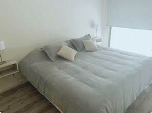 Un dormitorio con cama, almohadas, una mesita de noche y una lámpara.