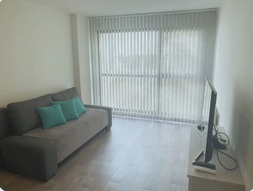 A living room with a sofa, a television, and a window with blinds.