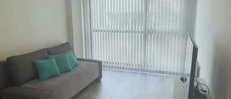 A living room with a sofa, a television, and a window with blinds.