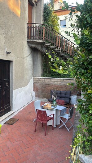 An outdoor patio with a table and chairs, a small garden area, and a staircase leading to an upper level.