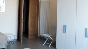 Ein Schlafzimmer mit einem Bett, einem Kleiderschrank, einem Heizkörper und einer Tür zu einem anderen Raum.