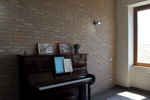 Un piano avec des partitions et des livres, un mur de briques et une fenêtre laissant entrer la lumière naturelle.