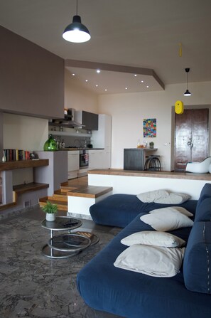 A modern living room with a blue sofa, a coffee table, and a kitchen area in the background.