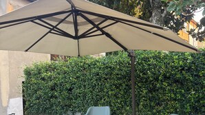 Eine Terrasse mit künstlichem Rasen, zwei grauen Plastikstühlen und einem großen, beigen Sonnenschirm.