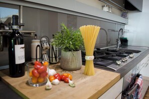 En köksbänk med en flaska, en växt, spaghetti och några grönsaker.