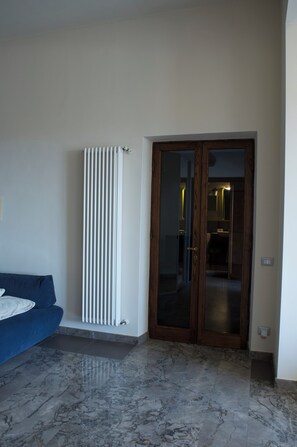 Una habitació amb un sofà blau, un radiador blanc i una porta de fusta amb panells de vidre.