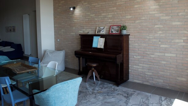 A room with a piano, a glass table, and a brick wall.