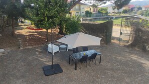 Un patio al aire libre con una mesa, sillas, un paraguas blanco y un árbol.