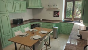 A kitchen with green cabinets, a granite countertop, a dining table set with plates and glasses, and a window with a view of greenery. - Room in Ponte da Barca (Vila Nova de Muía)