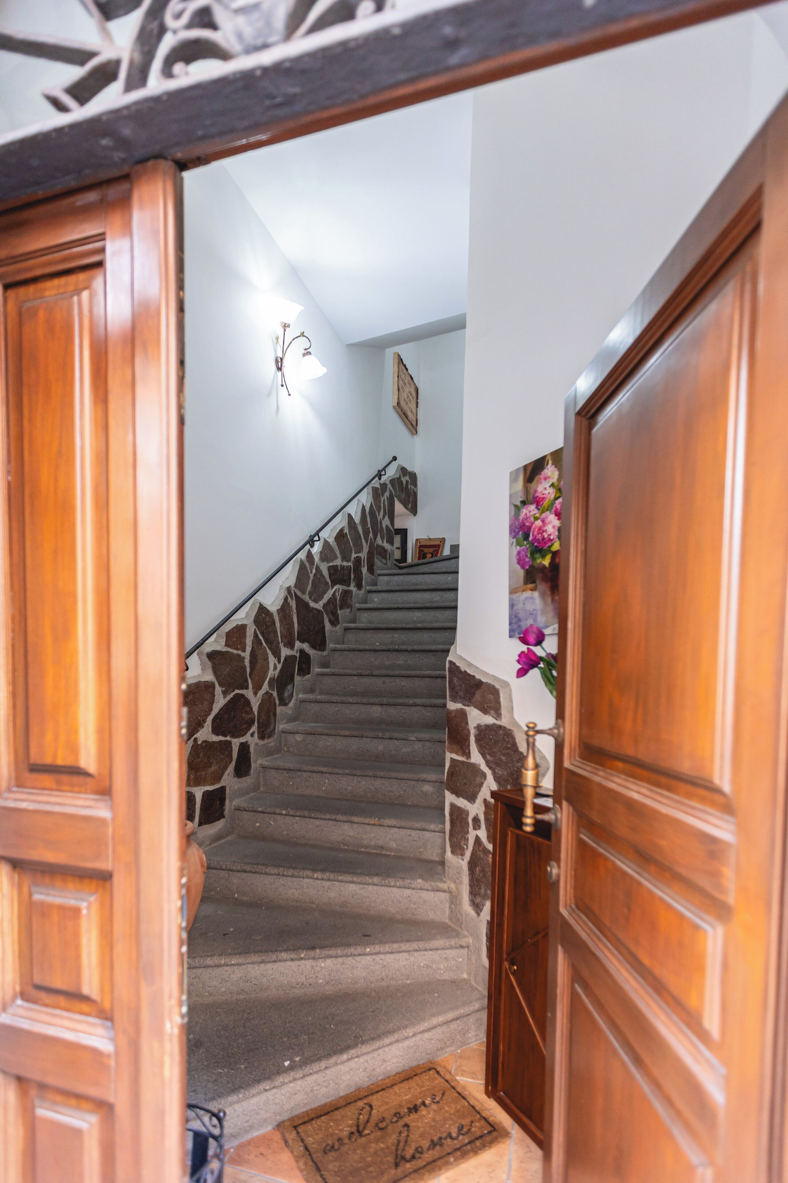 Una scala in legno con dettagli in pietra che conduce a un pianerottolo con un tappetino d'ingresso.