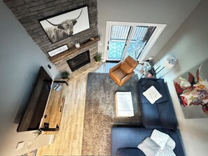 Ein modernes Wohnzimmer mit Kamin aus Stein, einem großen Flachbildfernseher, einem blauen Sofa und einem gemusterten Teppich.