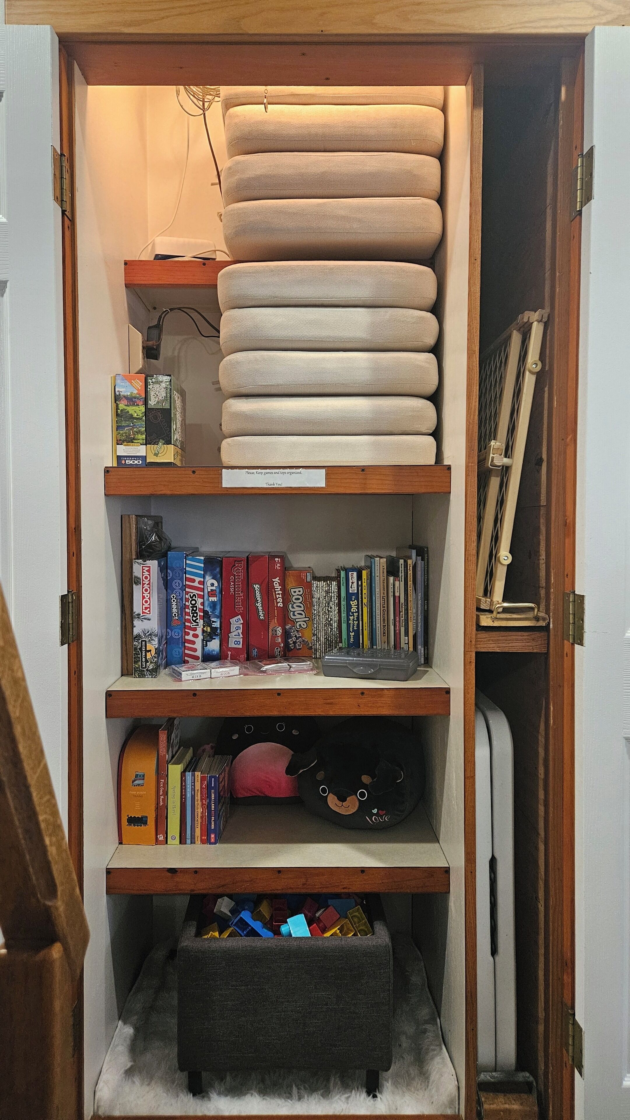 Un espace de rangement doté d’étagères contenant des jeux de société, des livres et un jouet en peluche.