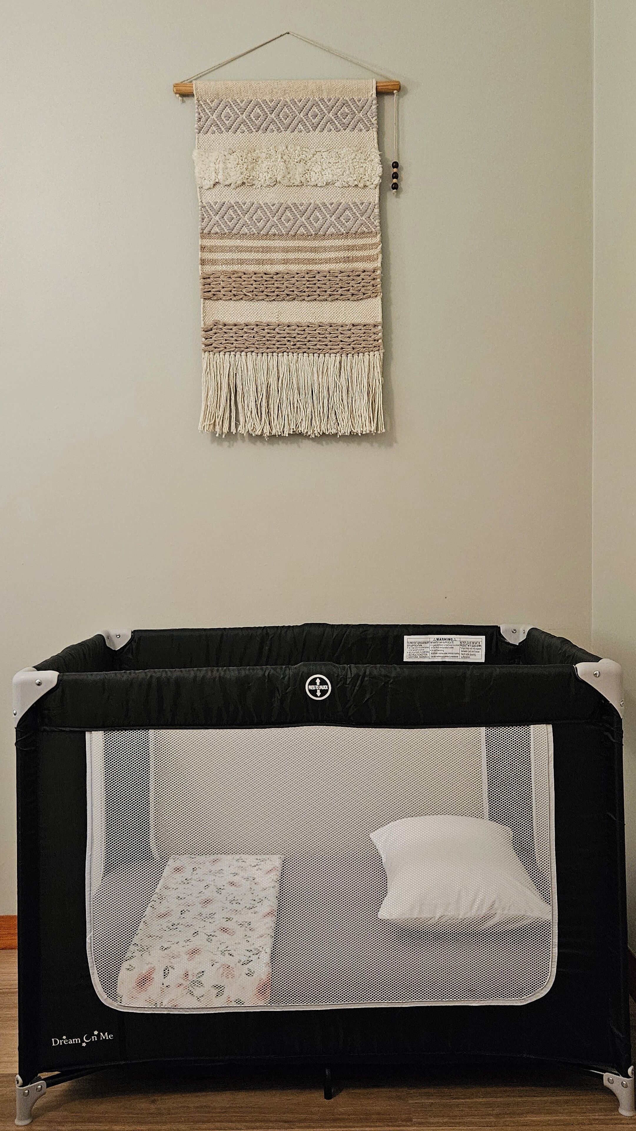 A crib with a mesh side and a patterned blanket hanging above it.