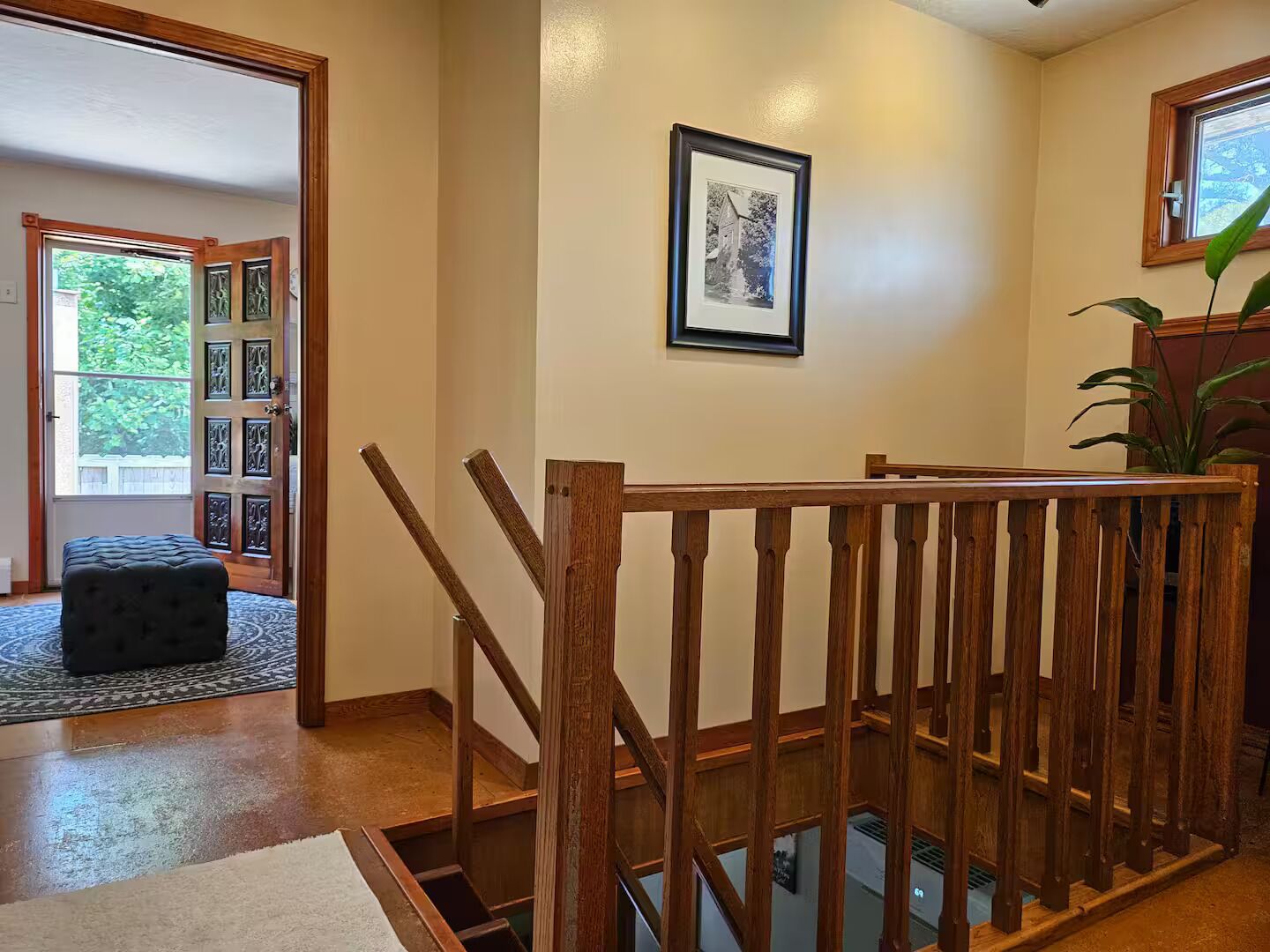 Uma escada de madeira com corrimão, um quadro emoldurado na parede e um vaso com planta.