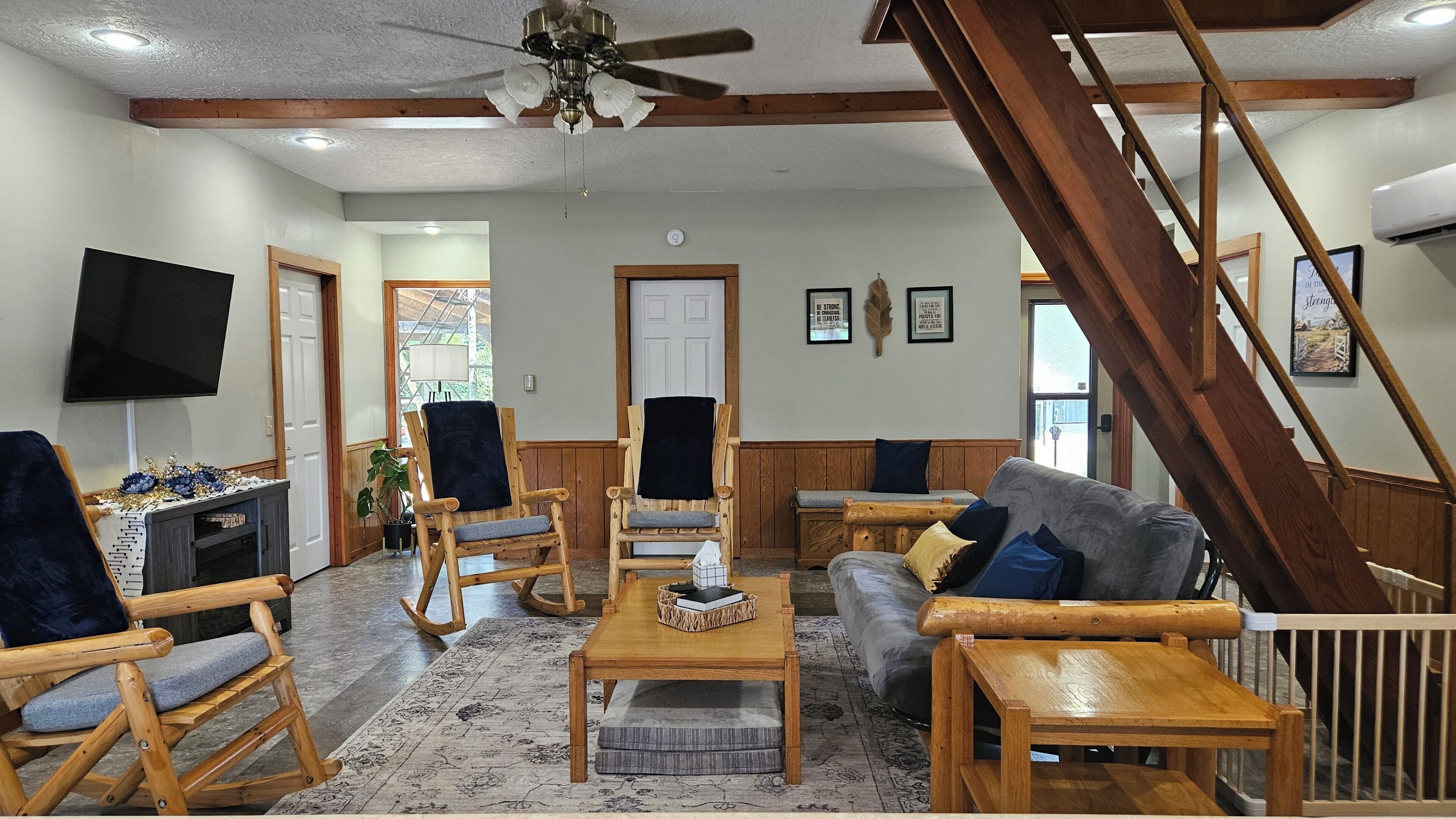 A spacious living room with a wooden staircase, a flat-screen TV, and a fireplace.