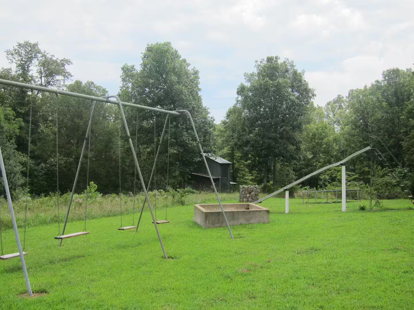 A grassy outdoor area with a swing set and a concrete structure.