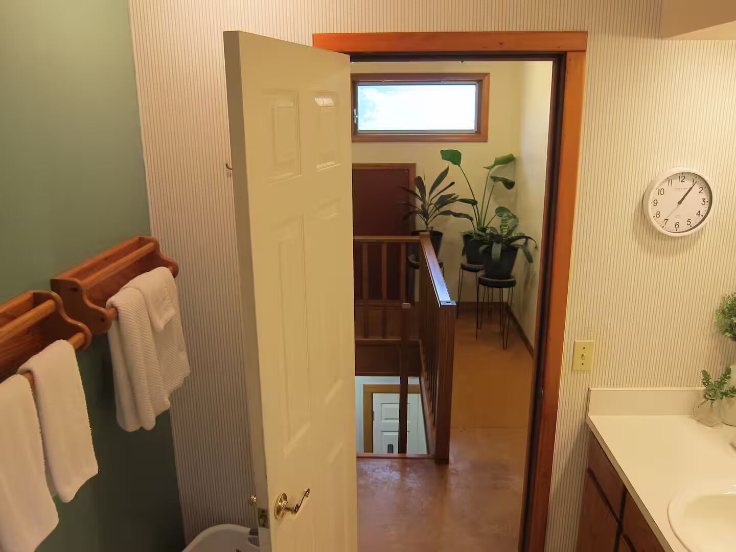 Un baño con un toallero de madera, un lavamanos blanco y un reloj en la pared.
