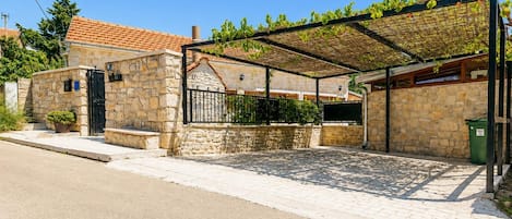 Un bâtiment en pierre avec un toit en tuiles, un espace extérieur couvert délimité par une clôture en métal et une allée pavée.