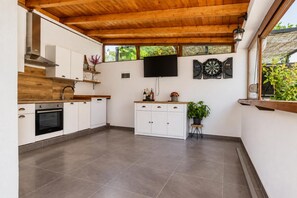 A modern kitchen with a wooden ceiling, a built-in oven, white cabinets, a flat-screen TV, and a dartboard. - Villa Ika - Two Bedroom Villa, Sleeps 4 (Raštević)