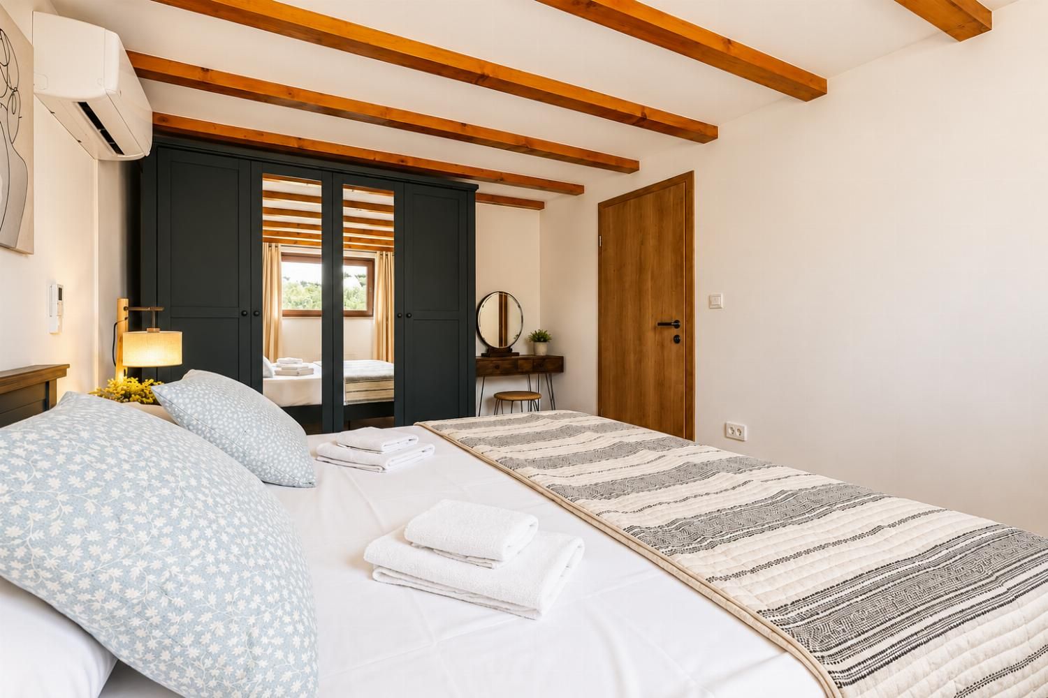 Bright double bedroom with warm wooden ceiling beams, contemporary furnishings, and soft neutral decor.