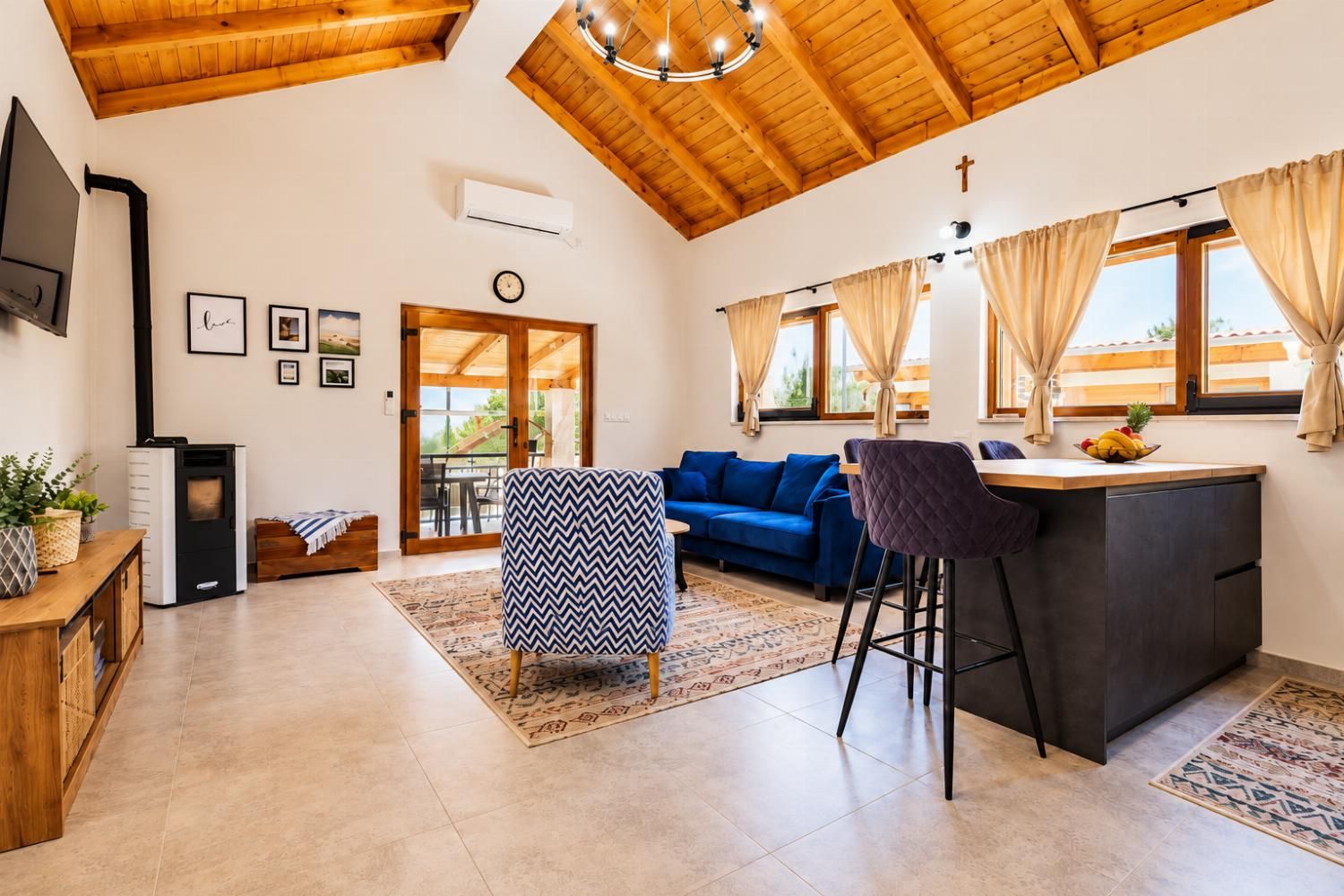 Bright open-plan lounge and dining space with wooden ceiling, modern seating, TV, and warm Mediterranean styling.