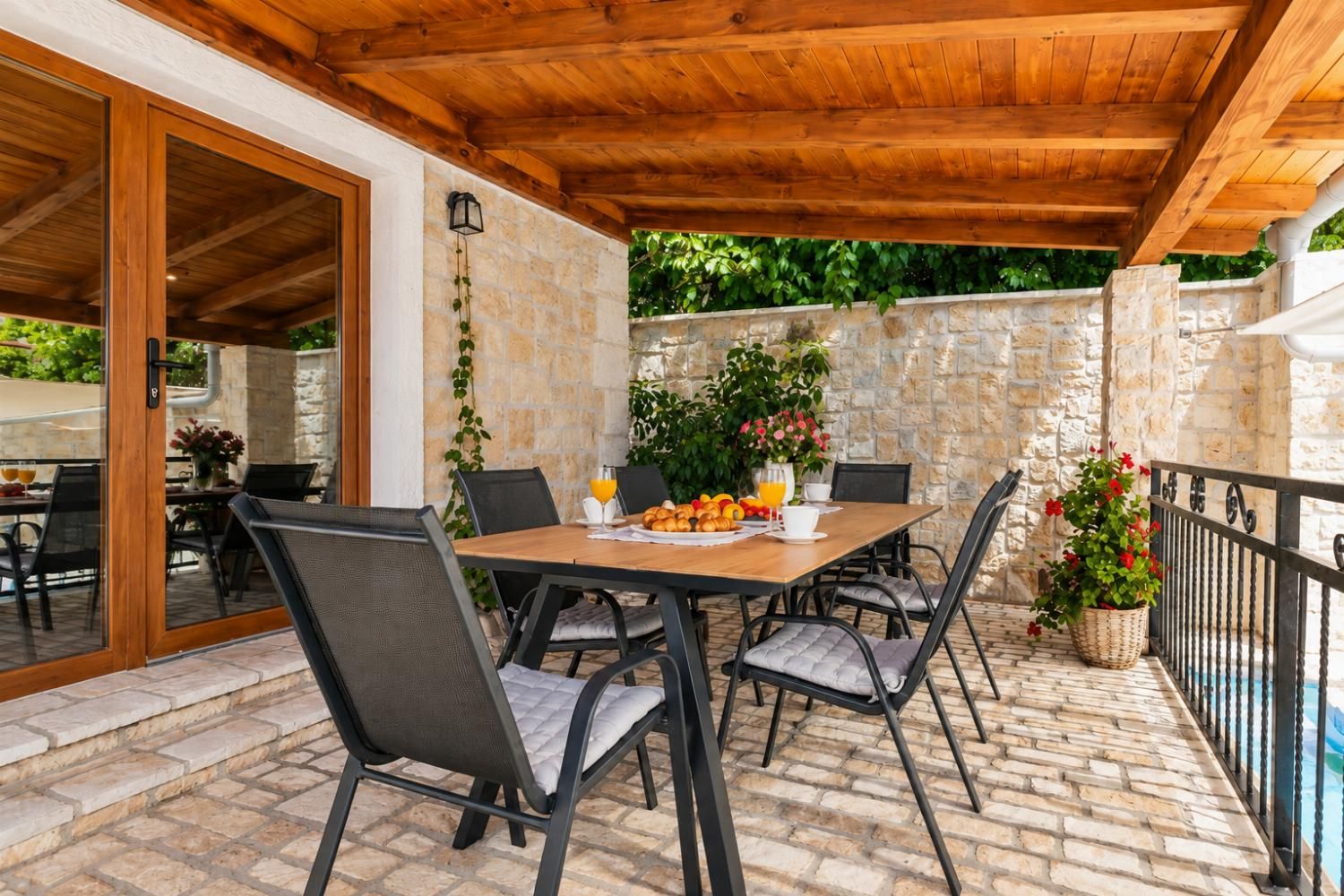 An outdoor patio with a wooden table set for breakfast, surrounded by chairs.