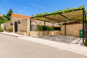 A stone building with a tiled roof, a covered outdoor area with a pergola, and a paved driveway. - Villa Ika - Two Bedroom Villa, Sleeps 4 (Raštević)