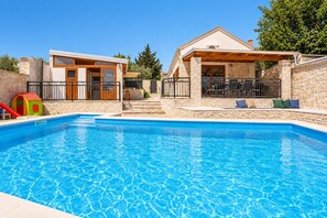 A swimming pool with a wooden deck and stone walls, a children's play area, and a covered outdoor seating area. - Villa Ika - Two Bedroom Villa, Sleeps 4 (Raštević)