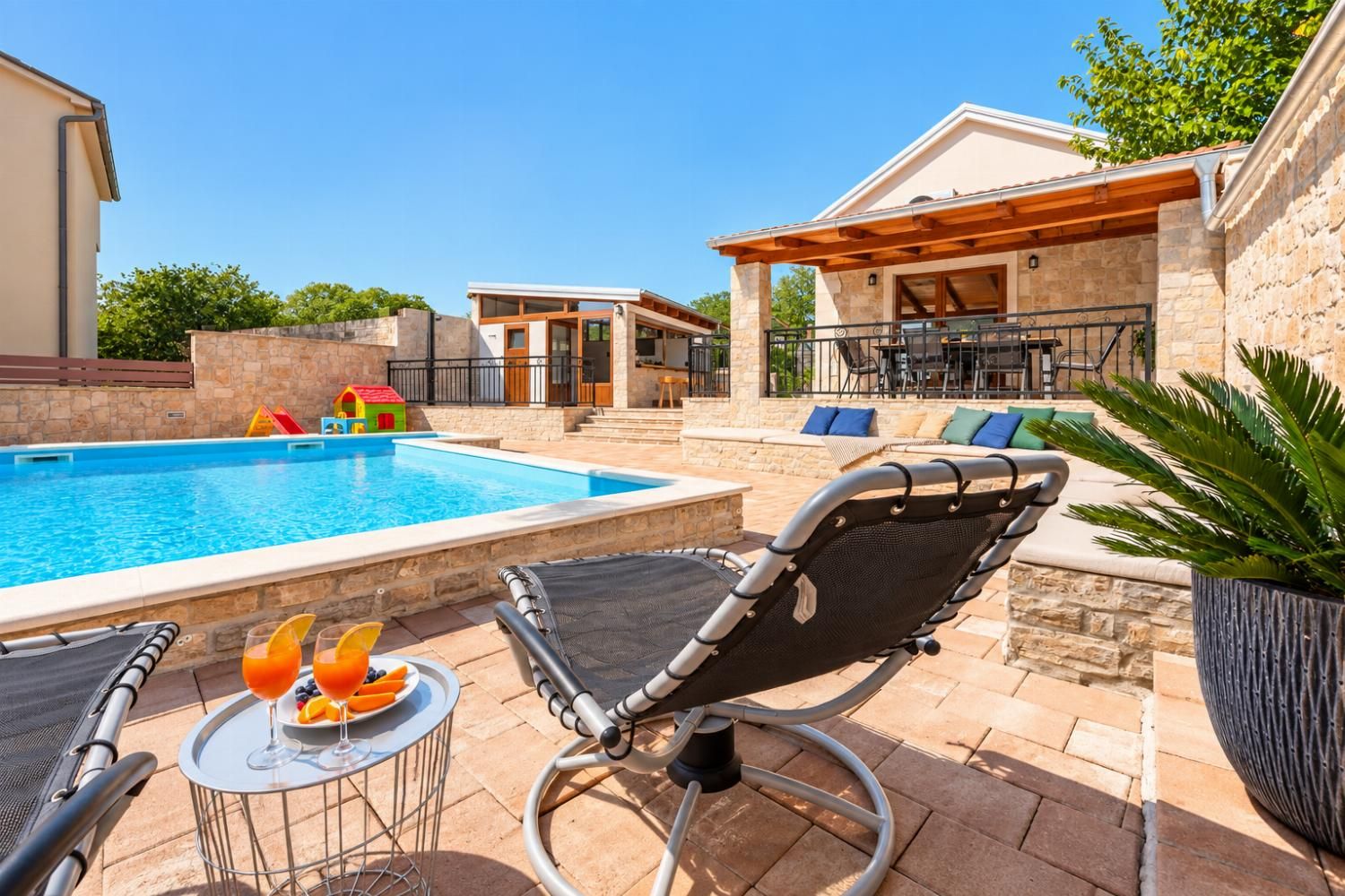 A poolside area with lounge chairs, a small table with drinks, and a stone building in the background.