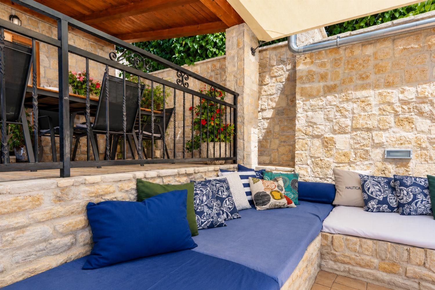 Un espace extérieur aménagé avec des murs en pierre, une terrasse couverte et une table entourée de chaises.