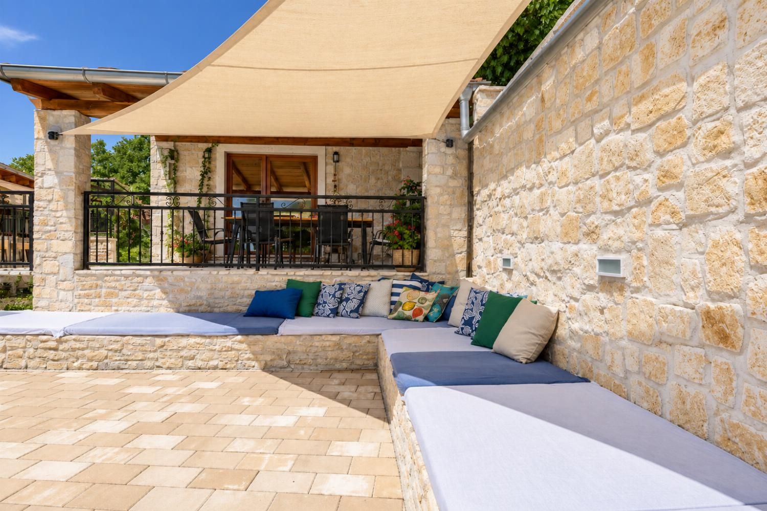 A stone-walled outdoor seating area with a covered patio, stone flooring, and a view of the surrounding landscape.