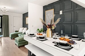 Ein Essbereich mit einem weißen Tisch, der für eine Mahlzeit gedeckt ist, einer grünen Couch im Hintergrund und einer dunkelwandigen Verkleidung.