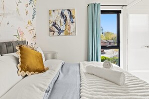 A bedroom with a bed, a window with curtains, a radiator, and a wall with a floral pattern. - 3BR Contractor House By ELS Property Group Salford (Salford)